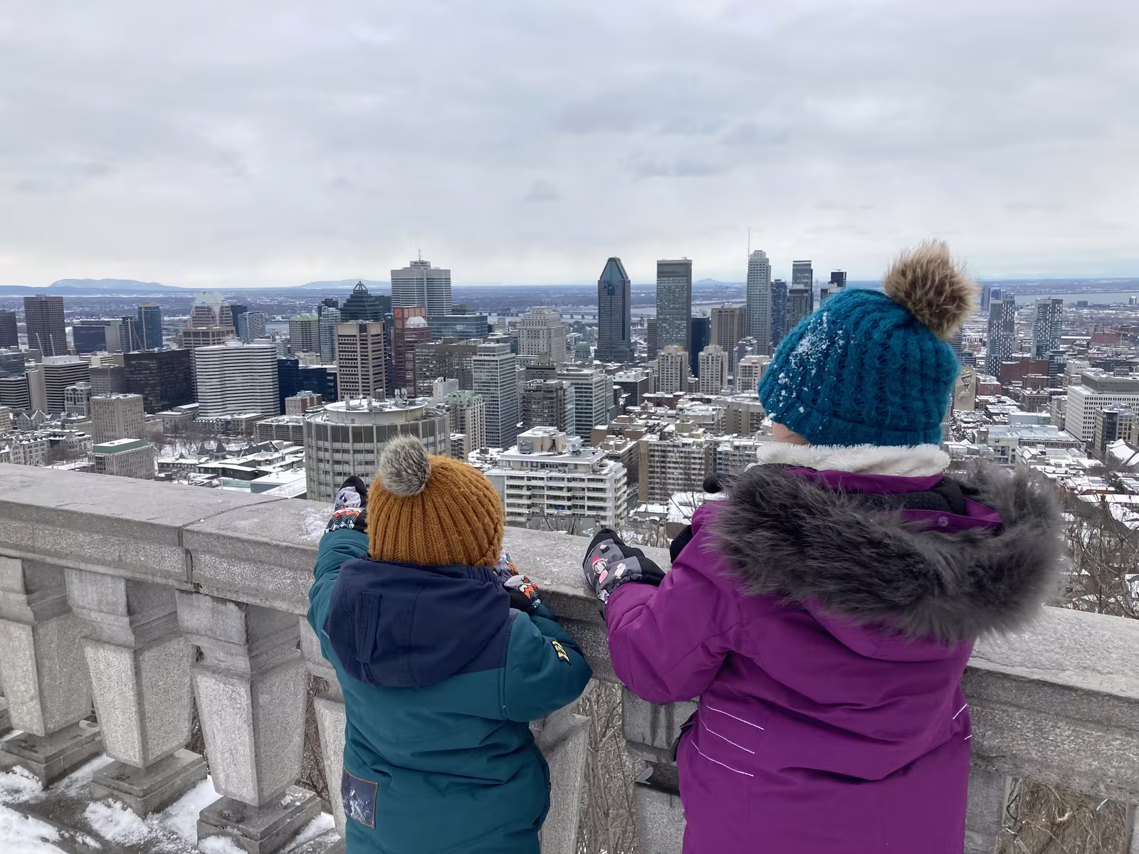Deux enfants observant les gratte-ciel de Montréal enneigés depuis le mont Royal en hiver