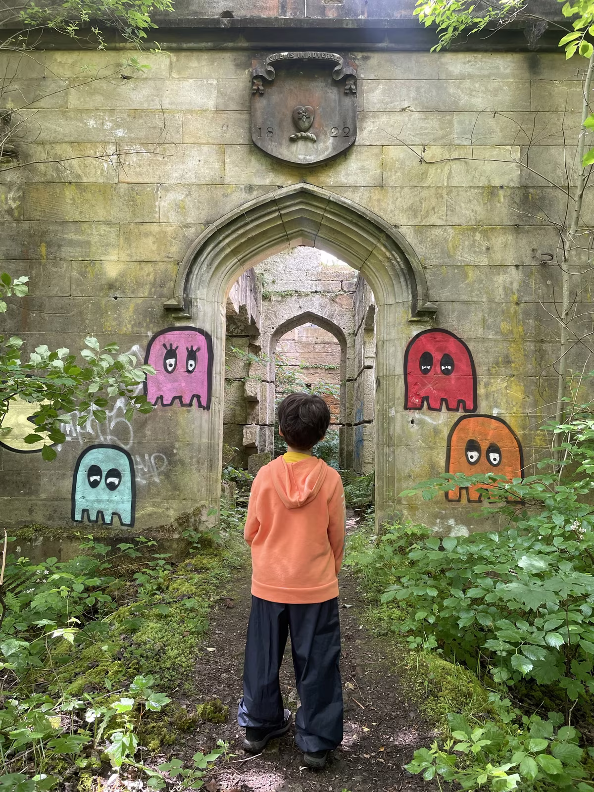 Enfant devant une arche en ruines avec des graffitis de fantômes colorés dans une forêt écossaise