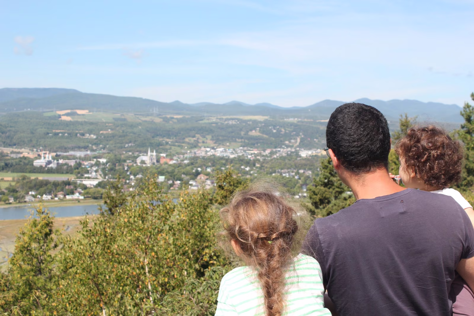 Famille admirant depuis un belvédère un village au bord du fleuve, au pied des montagnes