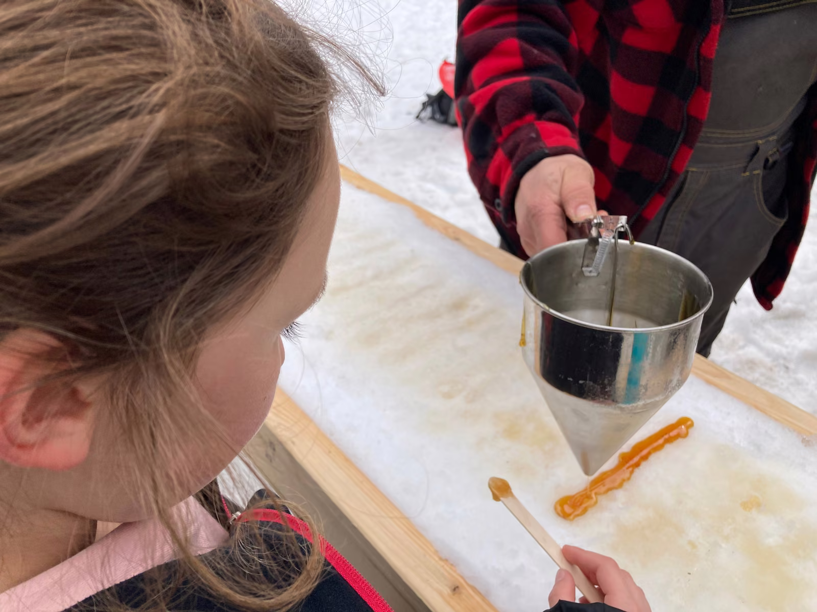 Enfant regardant la tire d'érable coulée sur la neige dans une cabane à sucre